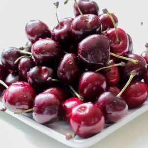 A pile of ripe, juicy red cherries on a white plate, showcasing their freshness.